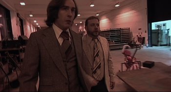 Movie still from “24 Hour Party People” (2002), directed by Tom Bruggen – A couple of men standing next to each other in a room; Medium shot, Low angle
