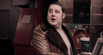 Movie still from “24 Hour Party People” (2002), directed by Tom Bruggen – A man in a leather jacket and a fur stole; Close Up shot, Over the shoulder angle