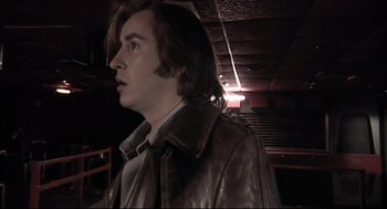 Movie still from “24 Hour Party People” (2002), directed by Tom Bruggen – A man in a leather jacket standing next to a stage; Close Up shot, Low angle
