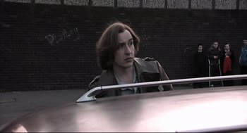 Movie still from “24 Hour Party People” (2002), directed by Tom Bruggen – A man sitting in the back seat of a car; Medium shot, Low angle