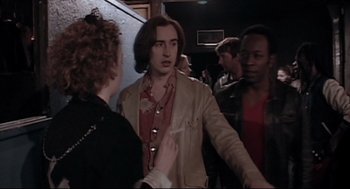 Movie still from “24 Hour Party People” (2002), directed by Tom Bruggen – A group of people standing around a room; Medium shot, Over the shoulder angle