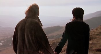 Movie still from “24 Hour Party People” (2002), directed by Tom Bruggen – Two people holding hands while standing on top of a hill; Wide shot, High angle
