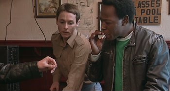 Movie still from “24 Hour Party People” (2002), directed by Tom Bruggen – Two men sitting in front of each other talking on a cell phone; Medium shot, Over the shoulder angle