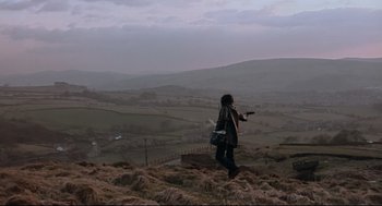 Movie still from “24 Hour Party People” (2002), directed by Tom Bruggen – A person standing on top of a hill holding a gun; Extreme Wide shot, High angle