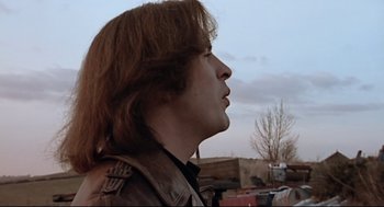 Movie still from “24 Hour Party People” (2002), directed by Tom Bruggen – A man with long brown hair wearing a leather jacket; Close Up shot, Low angle