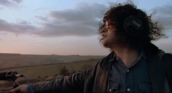 Movie still from “24 Hour Party People” (2002), directed by Tom Bruggen – A man with headphones standing on top of a hill; Medium shot, Low angle
