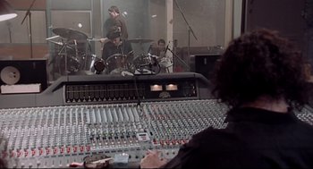 Movie still from “24 Hour Party People” (2002), directed by Tom Bruggen – A woman sitting at a mixing board in a recording studio; Wide shot, High angle