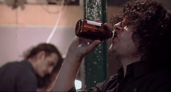 Movie still from “24 Hour Party People” (2002), directed by Tom Bruggen – A man is drinking a beer from a bottle; Close Up shot, Low angle