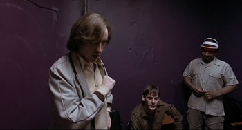 Movie still from “24 Hour Party People” (2002), directed by Tom Bruggen – Two men sitting next to each other on a purple wall; Medium shot, Low angle
