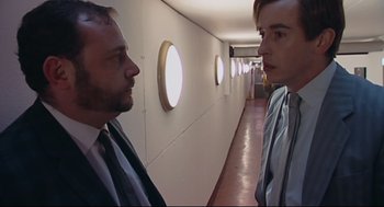 Movie still from “24 Hour Party People” (2002), directed by Tom Bruggen – Two men in business suits are standing in a hallway; Medium shot, Low angle