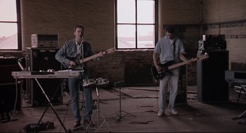 Movie still from “24 Hour Party People” (2002), directed by Tom Bruggen – Two men are playing instruments in an abandoned building; Wide shot, Low angle