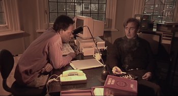 Movie still from “24 Hour Party People” (2002), directed by Tom Bruggen – Two men sitting at a table with a computer; Medium shot, High angle