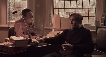 Movie still from “24 Hour Party People” (2002), directed by Tom Bruggen – Two men sitting at a table in front of a window; Medium shot, Low angle