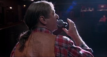 Movie still from “24 Hour Party People” (2002), directed by Tom Bruggen – A man with long hair is singing into a microphone; Close Up shot, Over the shoulder angle