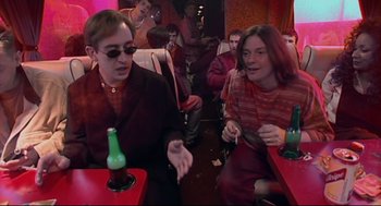 Movie still from “24 Hour Party People” (2002), directed by Tom Bruggen – A man and a woman sitting at a table with drinks; Medium shot, High angle