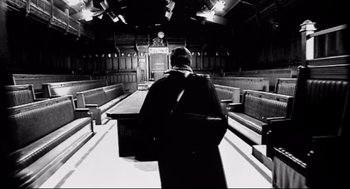 Movie still from “24 Hour Party People” (2002), directed by Tom Bruggen – A man in a black robe standing in front of benches; Wide shot, Low angle