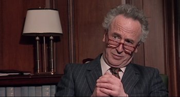 Movie still from “24 Hour Party People” (2002), directed by Tom Bruggen – An older man in a suit and glasses; Close Up shot, Over the shoulder angle