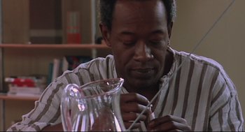 Movie still from “24 Hour Party People” (2002), directed by Tom Bruggen – A man is sitting in front of a glass pitcher; Close Up shot, Low angle