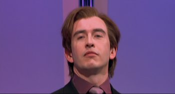 Movie still from “24 Hour Party People” (2002), directed by Tom Bruggen – A man with long brown hair wearing a suit and tie; Close Up shot, Low angle