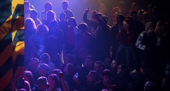 Movie still from “24 Hour Party People” (2002), directed by Tom Bruggen – A group of people sitting in a dark room; Wide shot, High angle