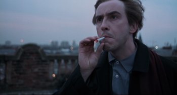 Movie still from “24 Hour Party People” (2002), directed by Tom Bruggen – A man smoking a cigarette while holding a cell phone to his ear; Close Up shot, Low angle