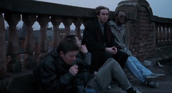 Movie still from “24 Hour Party People” (2002), directed by Tom Bruggen – A group of men sitting on a ledge; Medium shot, Low angle