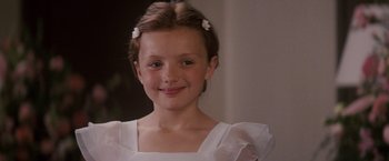 Movie still from “27 Dresses” (2008), directed by Anne Fletcher – A young girl wearing a white dress with white flowers in her hair; Close Up shot, Over the shoulder angle
