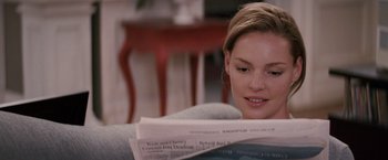 Movie still from “27 Dresses” (2008), directed by Anne Fletcher – A woman sitting on a couch reading a newspaper; Close Up shot, Over the shoulder angle