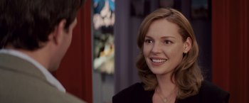 Movie still from “27 Dresses” (2008), directed by Anne Fletcher – A woman smiles at the camera in front of another woman; Close Up shot, Over the shoulder angle