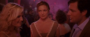 Movie still from “27 Dresses” (2008), directed by Anne Fletcher – A woman in a dress in front of a group of people; Close Up shot, Over the shoulder angle