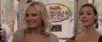 Movie still from “27 Dresses” (2008), directed by Anne Fletcher – A woman standing in front of a store window smiling; Close Up shot, Over the shoulder angle