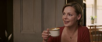 Movie still from “27 Dresses” (2008), directed by Anne Fletcher – A woman is holding a cup of coffee and smiling for the camera; Close Up shot, Over the shoulder angle