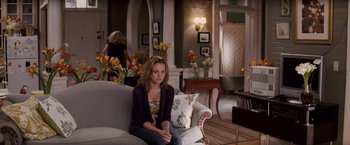 Movie still from “27 Dresses” (2008), directed by Anne Fletcher – A woman sitting on top of a couch in a living room; Wide shot, Over the shoulder angle