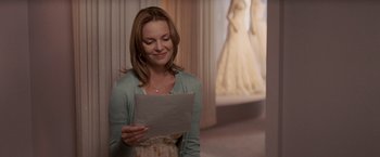 Movie still from “27 Dresses” (2008), directed by Anne Fletcher – A woman holding a piece of paper while standing in a room; Medium shot, Over the shoulder angle