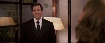 Movie still from “27 Dresses” (2008), directed by Anne Fletcher – A man in a suit and tie standing in front of a lamp; Medium shot, Over the shoulder angle