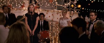Movie still from “27 Dresses” (2008), directed by Anne Fletcher – Two women and a man are singing in front of a microphone; Medium shot, Over the shoulder angle