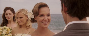 Movie still from “27 Dresses” (2008), directed by Anne Fletcher – A woman with a flower in her hair smiling; Close Up shot, Over the shoulder angle