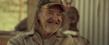 Movie still from “31” (2016), directed by Rob Zombie – An old man with long hair wearing a hat; Close Up shot, Over the shoulder angle