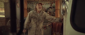 Movie still from “31” (2016), directed by Rob Zombie – An older man wearing a hat standing in front of a crowd; Medium shot, Low angle