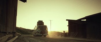 Movie still from “31” (2016), directed by Rob Zombie – A van with luggage on the back of it driving down a dirt road at sunset; Extreme Wide shot, Low angle
