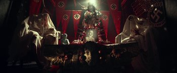 Movie still from “31” (2016), directed by Rob Zombie – A group of people sitting in a room with nazi flags on the wall; Wide shot, High angle