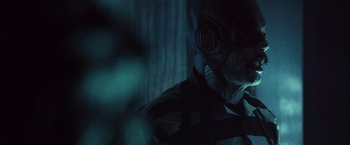 Movie still from “31” (2016), directed by Rob Zombie – A person wearing a mask in a dark room; Close Up shot, Over the shoulder angle