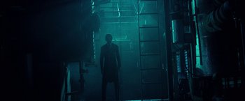 Movie still from “31” (2016), directed by Rob Zombie – A man standing in a dark room in front of a ladder; Wide shot, Low angle