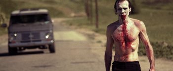 Movie still from “31” (2016), directed by Rob Zombie – A shirtless man with blood all over his face; Medium shot, Over the shoulder angle