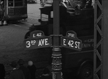 Movie still from “42nd Street” (1933), directed by Lloyd Bacon – A black and white photo of a street pole with street signs; Extreme Wide shot, High angle