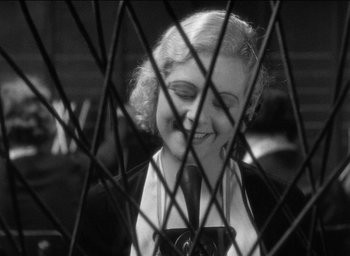 Movie still from “42nd Street” (1933), directed by Lloyd Bacon – A black - and - white photo of a woman looking through a fence; Close Up shot, Over the shoulder angle
