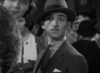 Movie still from “42nd Street” (1933), directed by Lloyd Bacon – A man in a suit and tie with a hat on; Close Up shot, Over the shoulder angle