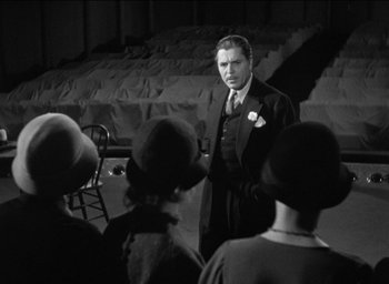 Movie still from “42nd Street” (1933), directed by Lloyd Bacon – A man standing in front of a group of people; Wide shot, Over the shoulder angle