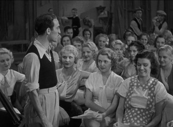 Movie still from “42nd Street” (1933), directed by Lloyd Bacon – An old black and white photo of a group of people; Medium shot, Over the shoulder angle