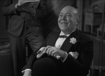 Movie still from “42nd Street” (1933), directed by Lloyd Bacon – An older man in a tuxedo sitting in a chair; Close Up shot, Low angle